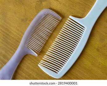 Close-up top view of two different plastic hair combs, one white and one translucent purple, lying side by side on a textured wooden table surface, representing everyday grooming tools and personal care items