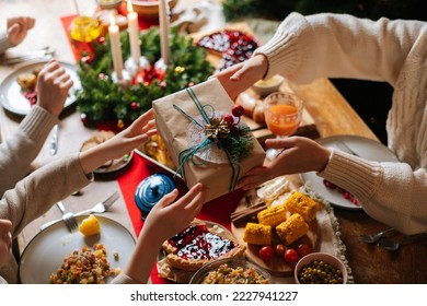 Close-up top view of unrecognizable loving parent giving festive box with Christmas present to happy son sitting at dinner feast table during holiday family party, selective focus, blurred background - Powered by Shutterstock