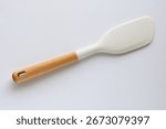 A closeup, top-down studio shot of a modern white silicone spatula with a wooden handle, isolated on a clean white background.