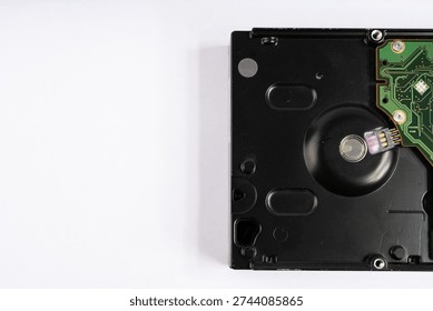 A close-up, top-down view of the back of a computer hard drive, revealing its intricate green circuit board (PCB) with various components and connectors. The black housing of the hard drive is partially visible, creating a strong contrast against the clean, bright white background. The image highlights the detailed electronic architecture essential for data storage and processing, presented with even, soft lighting.