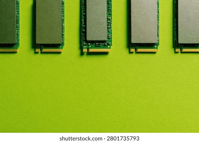 A close-up, top-down view of five NVMe M.2 SSDs arranged in a neat row against a bright, solid green backdrop.