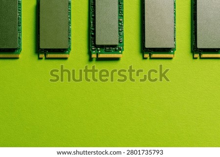 A close-up, top-down view of five NVMe M.2 SSDs arranged in a neat row against a bright, solid green backdrop.