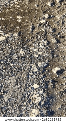 Close-up, top-down view of a gritty, textured ground surface. A mix of wet sand, gravel, and broken stones creates a natural, earthy, and abstract background.