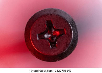 A close-up, top-down view of a Phillips head screw against a pink and red gradient background.