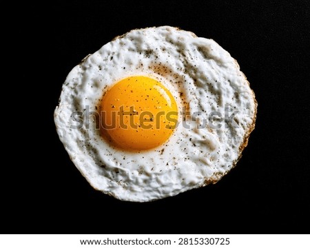 A close-up, top-down view of a single, freshly fried egg with a vibrant, unbroken yolk, set against a stark black backdrop.