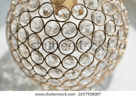 Close-up, top-down view of a spherical light fixture or decorative object, adorned with numerous clear crystal facets set in interconnected golden rings