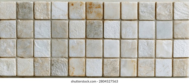 A close-up, top-down view of a textured surface composed of numerous small, square mosaic tiles made from natural stone.