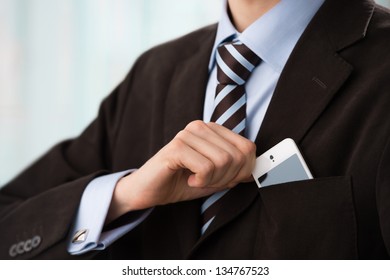 Closeup of torso of confident business man wearing elegant suit taking mobile phone from pocket