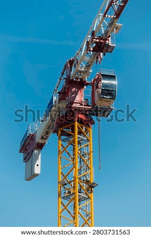 Close-up of a tower crane operator cabin and counterweight high above a construction site against a deep blue sky.