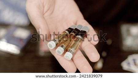 Close-up of transparent containers with CBD oil in hand. Tanks for vape with Durability and Resistance to Temperature Changes. Considered alternatives to traditional smoking.