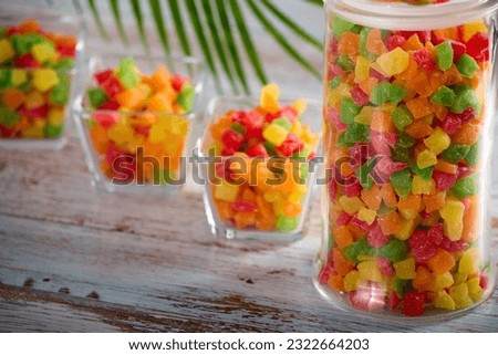 Close-up transparent glass jar and bowls are filled with colorful delicious candied fruits. Healthy sweet snack of candied fruits in a glass dish on a wooden table