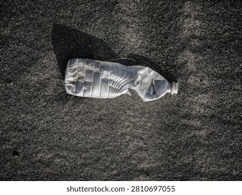 Close-up of a transparent plastic bottle filled with natural sand and covered with water droplets, placed on sandy ground under bright daylight. Natural texture with a minimal composition and copy space.