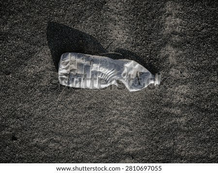 Close-up of a transparent plastic bottle filled with natural sand and covered with water droplets, placed on sandy ground under bright daylight. Natural texture with a minimal composition and copy space.