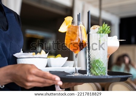 Closeup of tray with cocktails and appetizers - Spritz and mojito served by an African waitress in the restaurant bar