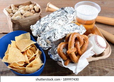 Closeup Of A Tray Of Food And Souvenirs That One Would Find At A Baseball Game. Items Include, Hot Dogs Wrapped In Foil, Beer, Peanuts, Chips, Baseball, Mini Bats And Pretzels. Horizontal Format.