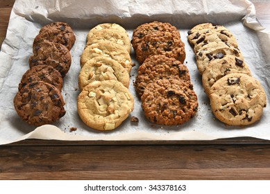 Closeup of a tray of fresh baked cookies, Chocolate Chip, oatmeal raisin Chocolate and white chocolate chip cookies on baking sheet and parchment paper.