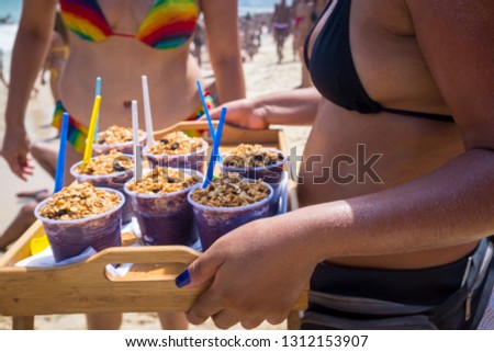 Close-up of a tray of frozen açaí berry snack served ready to eat with granola in disposable cups by an unrecognizable woman in a bikini on Ipanema Beach in Rio de Janeiro, Brazil