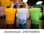 Closeup of tree delicious white, yellow and green boba milk tea or Taiwan milk tea drinks with boba bubbles or tapioca pearls at the bottom in plastic cups