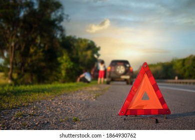 Close-up of triangular road warning sign with couple standing in front of broken car. at sunset - Shutterstock ID 1864930762