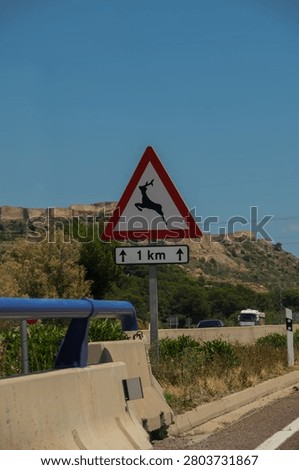 Close-up of a triangular warning traffic sign for wild animals crossing with an ancient fortress on a hill background in Spain.