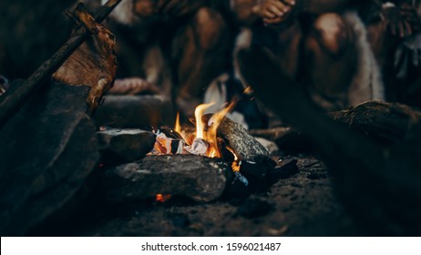 Close-up of Tribe Prehistoric Hunter-Gatherers Trying to Get Warm at the Bonfire, Holding Hands over Fire, Cooking Food. Neanderthal or Homo Sapiens Family Live in Cave at Night.