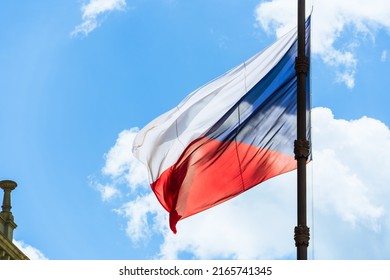 Close-up of the tricolor national flag of the Czech Republic on a bronze flagpole against a blue sky and white clouds on a sunny day in Prague, Czech symbols
