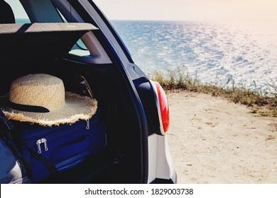 Close-up of the trunk of a car with suitcase and straw hat in it on the background of the sea. Travel concept