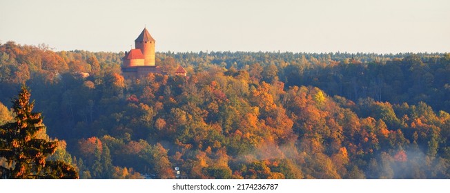 Close-up Of The Turaida Castle Tower In A Clouds Of Morning Fog At Sunrise. Colorful Red, Orange And Yellow Trees Of The Autumn Forest. Gauja National Park, Latvia. Travel Guide, Sightseeing Theme