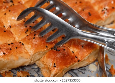 Close-Up of Turkish Cheese Borek with Black Sesame Seeds – Flaky Pastry with Serving Tongs, Ideal for Food Photography and Mediterranean Cuisine Concepts - Powered by Shutterstock