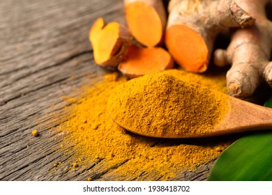 Close-up Turmeric (curcumin) powder in wooden spoon with fresh rhizome on wood background.