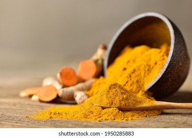 Close-up Of Turmeric (curcumin) Powder In  Wooden Spoon With Bowl And Fresh Rhizome Slices On Wood Background.