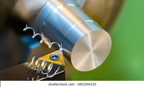 Closeup Of Turning Cylindrical Workpiece Of Aluminum Alloy On A Lathe Machine. Black Cutting Tool Bit With Yellow Triangular Carbide Insert And Two Beautiful Spiral Curled Metal Swarf. Chip Machining.