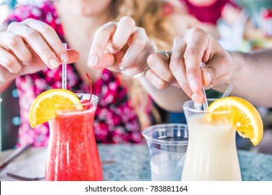Closeup of two alcoholic summer drinks, strawberry daiquiri and pina colada, in restaurant with people's hands touching, taking straws