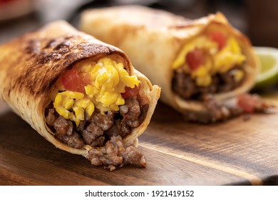 Closeup of two breakfast burritos with scrambled egg, sausage and tomato in a tortilla wrap