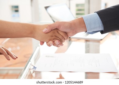 Close-up of two business partners shaking hands with each other near the contract lying on the table