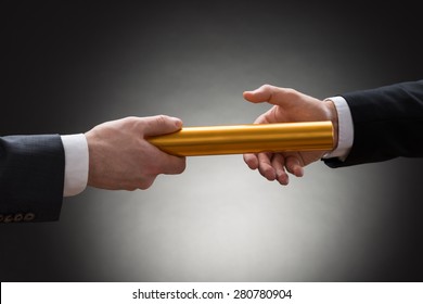 Close-up Of Two Businessman's Hand Passing A Golden Relay Baton