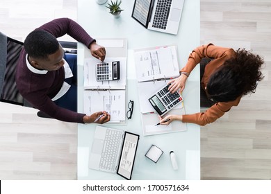 Close-up Of Two Businesspeople Calculating Financial Statement At Desk