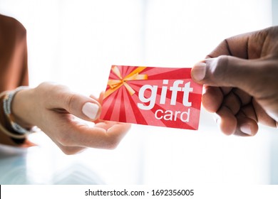 Close-up Of Two Businesspeople Hand Holding Red Gift Card