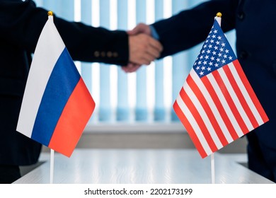 Close-up Of Two Businesspeople Shaking Hands In Front Of Us Russia Flags On Table