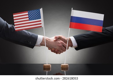 Close-up Of Two Businesspeople Shaking Hands In Front Of Us And Russia Flags On Table