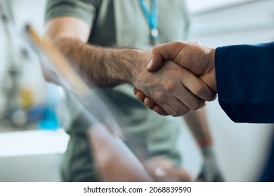 Close-up Of Two Car Mechanics Handshaking While Working In Repair Shop. 