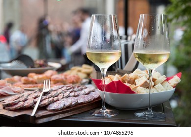 Closeup Of Two Cold Glasses Of White Wine Next To An Outdoor Food Buffet During A Party