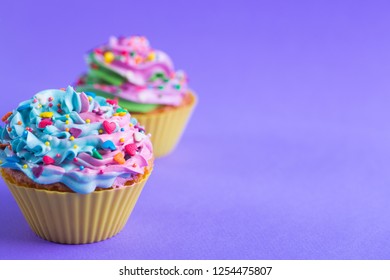 Closeup two colorful cupcakes decorated with sprinkles in shape of hearts on purple background with copy space. Multicolored romantic pastel desserts. - Powered by Shutterstock