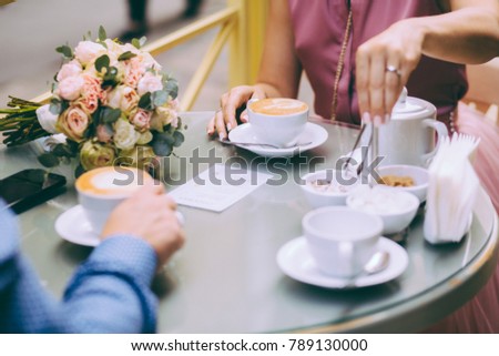 Close-up of two cups with cuppuccino. Unrecognizable bride and groom drinking coffee while sitting outdoor in round table.