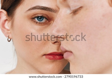 Closeup of two faces with focus on a female blue eye and natural skin texture. Woman and man with serious expression for portrait, emotions and human connection indoors.
