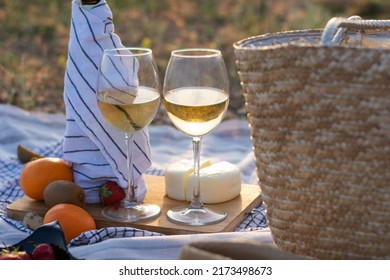 Close-up Of Two Glasses Of White Wine On The Background Of Cheese And A Bottle Of A Straw Bag Picnic In Summer In Nature At Sunset. Romantic Date. No People. White Wine. Concept: Alcohol And Drinks 