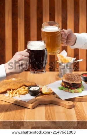 Closeup of two hands clinking beer stein glasses. Toasting with a pint of draft beers on counter at pub, raising toast with cold beer mugs at bar.