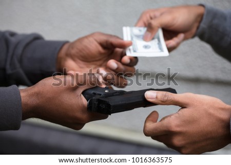 Close-up Of Two Hands Exchanging Black Handgun For Banknote