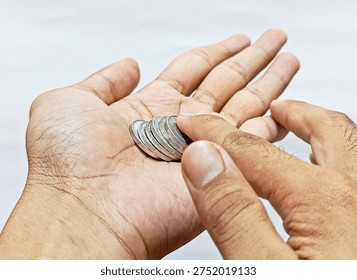 Close-up of two hands holding stack of silver coins on white background