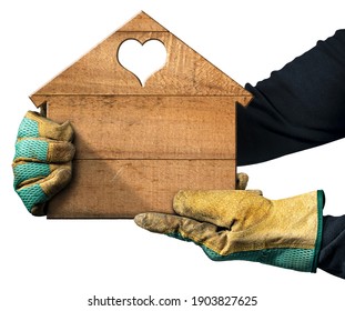 Closeup of two hands with protective work gloves holding a small wooden house with a heart-shaped hole. Isolated on white with copy space.